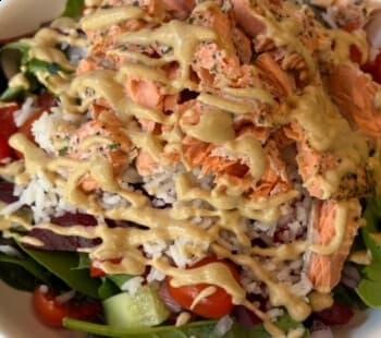A salad of salmon flakes, jasmine rice, spring mix, tomatoes and cucumber drizzled with a mustard dressing.