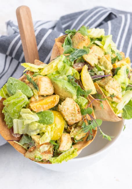Crispy tortilla cones filled with salad greens, diced chicken, avocado and cherry tomatoes in a white bowl.