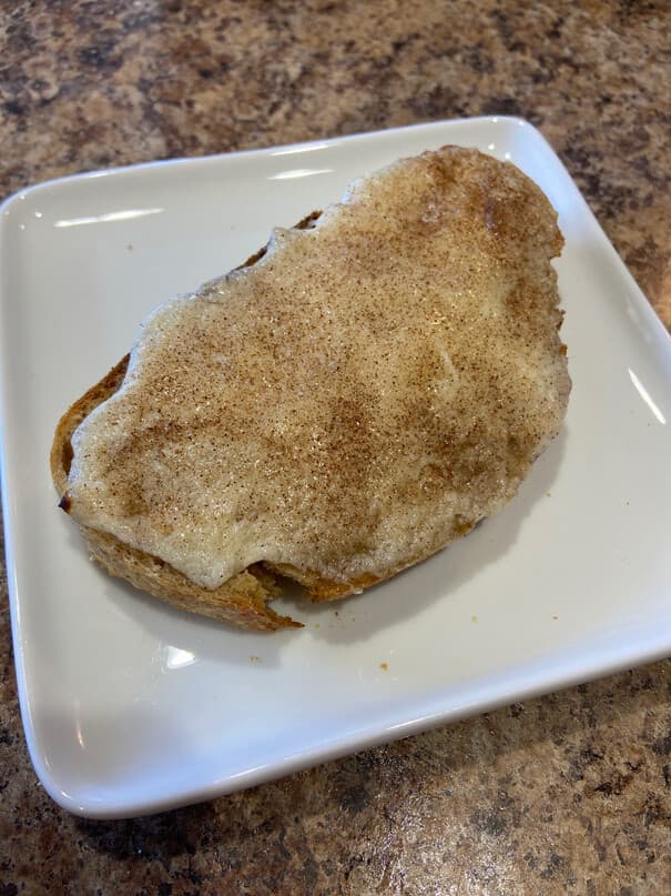 A slice of toast topped with melted cottage cheese and cinnamon sugar on a square white plate.