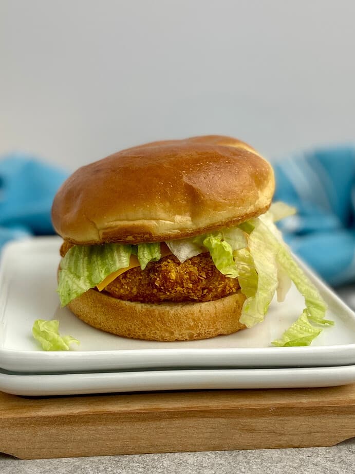 A crispy chicken burger with lettuce and cheese on a toasted bun, served on a white plate.