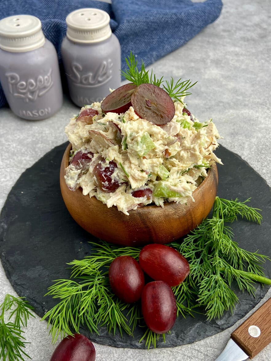 Chicken salad with grapes, celery and dill piled in a wooden bowl on a slate board.