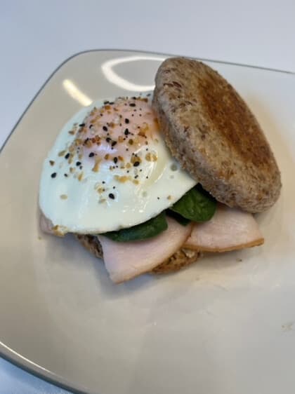 A breakfast sandwich on a toasted english muffin with a fried egg, spinach and smoked turkey on a white plate.