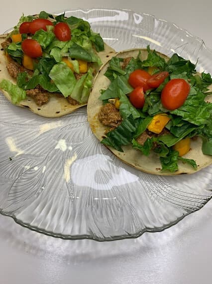 Two tostadas topped with seasoned ground beef, chopped romaine, butternut squash and cherry tomatoes on a glass plate.
