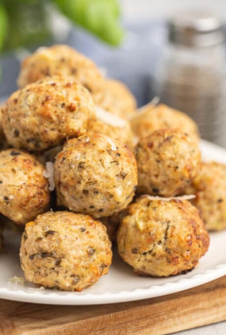 A pile of golden baked pesto turkey meatballs on a white plate.