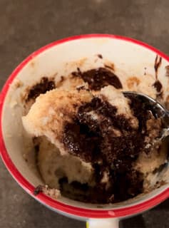 A red-rimmed mug of chocolate chip protein mug cake with a spoonful scooped out.